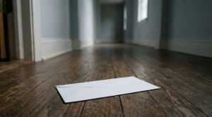 Unopened envelope on the floor of an empty home entry hall in morning light